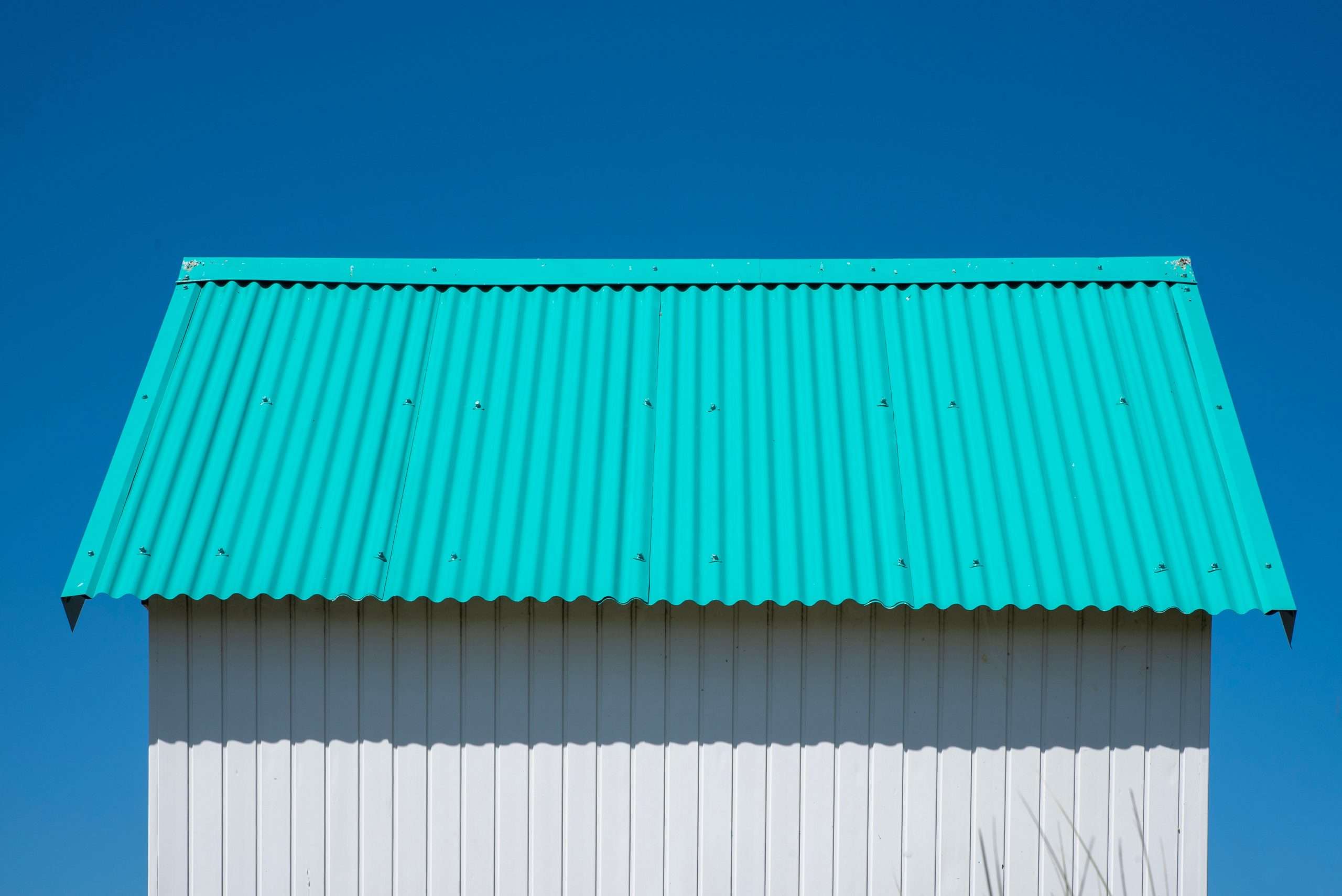 Close-up of a teal corrugated metal roof against a clear blue sky