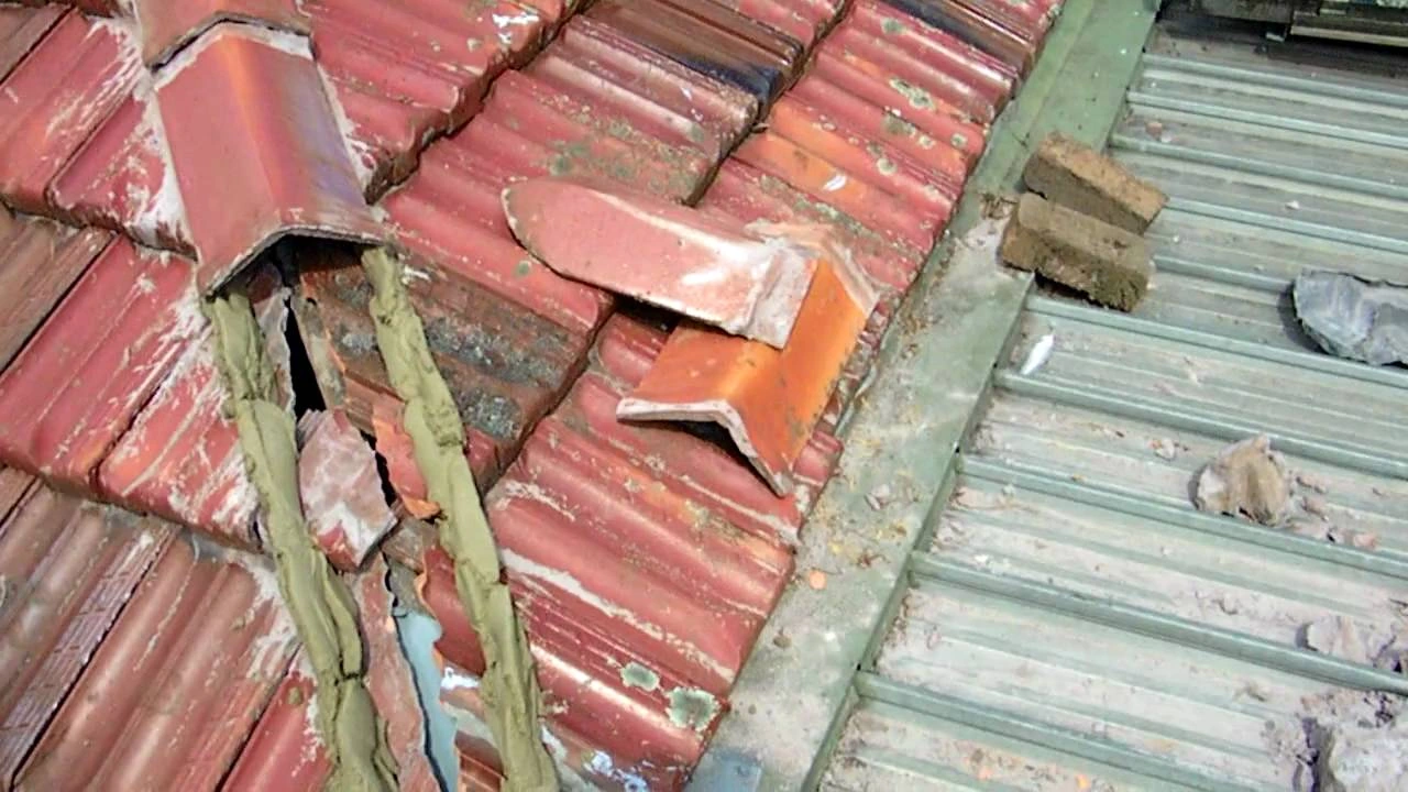 Damaged ridge caps and crumbling mortar on a tiled roof, indicating the need for re-bedding and repointing during roof restoration.